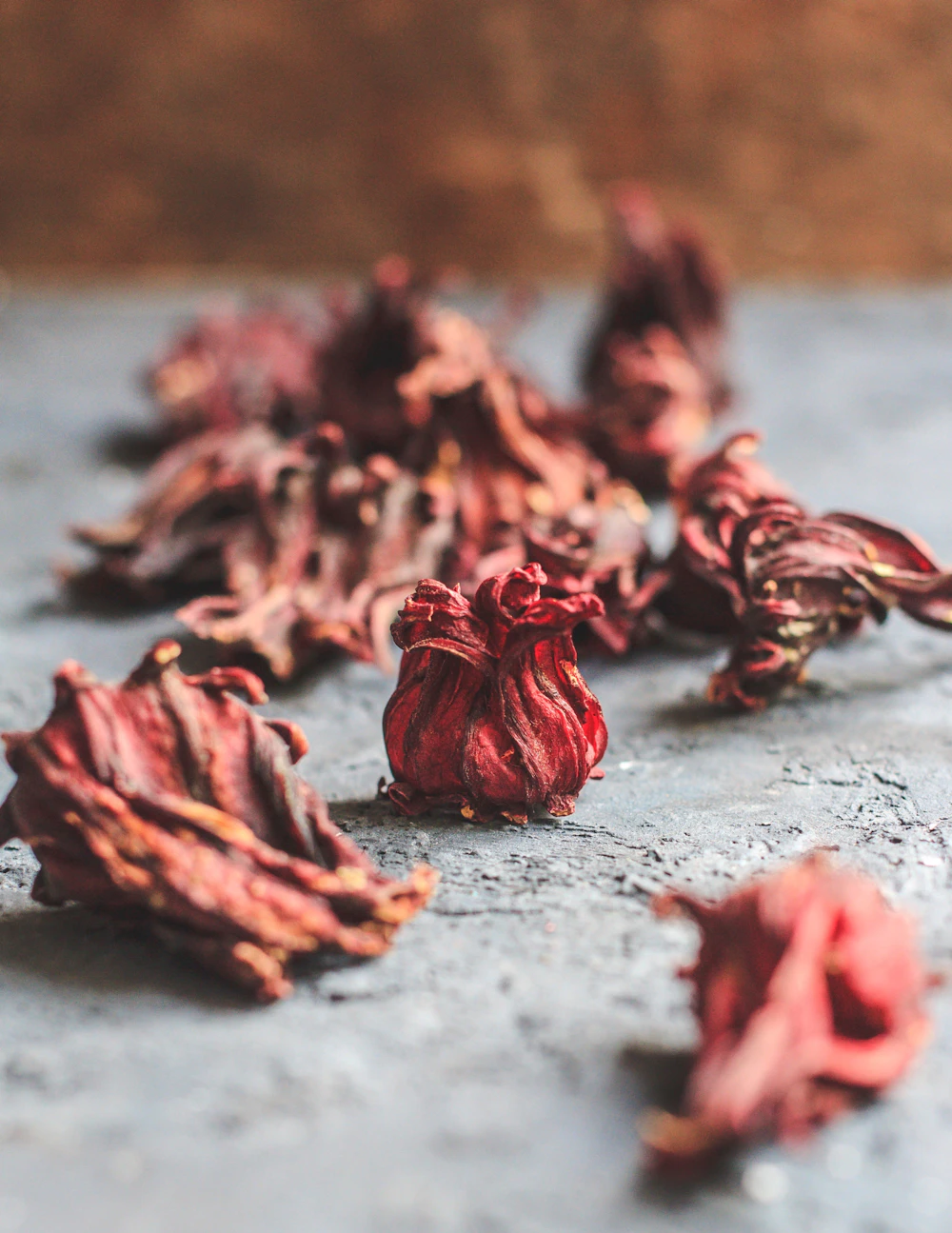Whole dried hibiscus calyces — deep crimson flor de jamaica — arranged on gray slate
