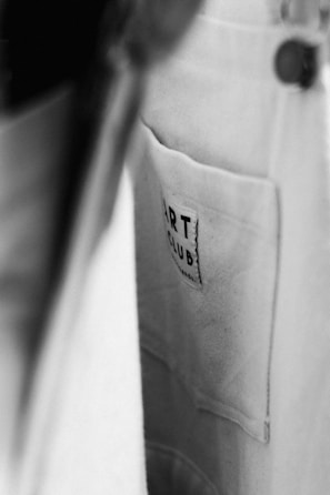 A close-up view of a fabric pocket with a label that reads 'ART CLUB'. The image is in black and white, with a focus on texture and contrast.