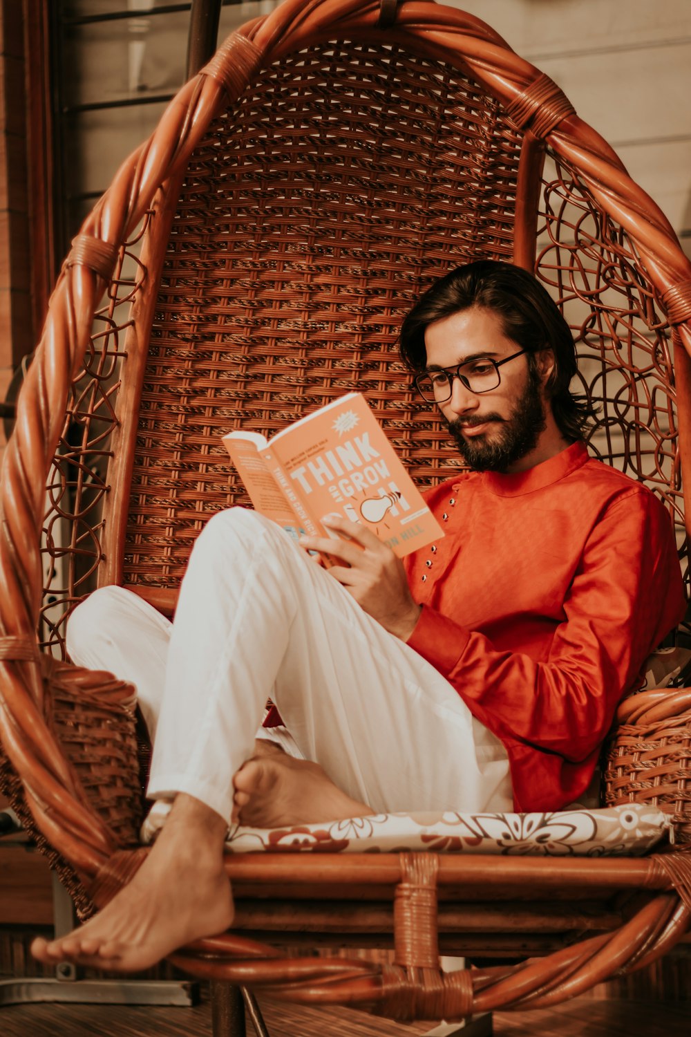 man in red long sleeve shirt and white pants sitting on brown woven chair