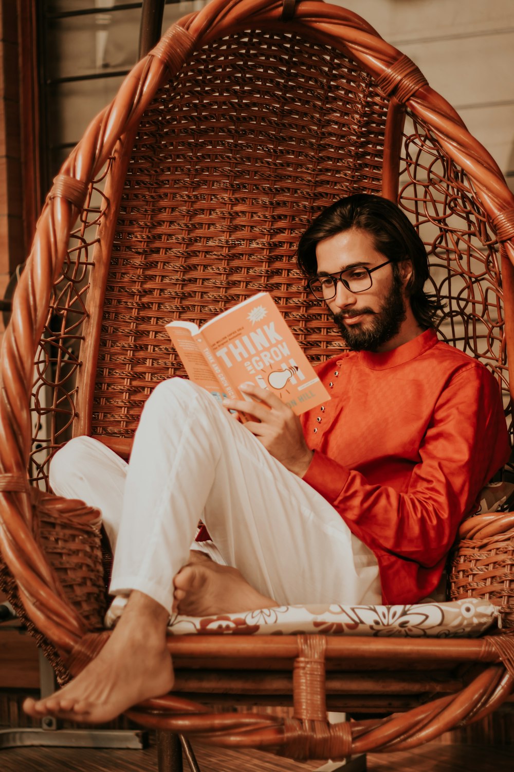Foto Hombre con camisa de manga larga roja y pantalón blanco sentado en una  silla tejida marrón – Imagen Lectura gratis en Unsplash
