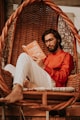 woman in red long sleeve shirt and white pants sitting on brown woven chair