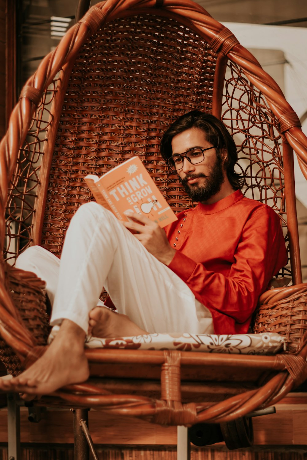 woman in red long sleeve shirt and white pants sitting on brown woven chair