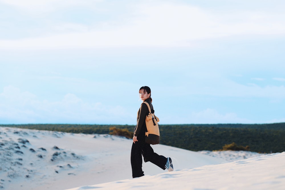 Frau in schwarzem Kleid, die tagsüber auf weißem Sand spazieren geht