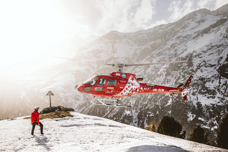 A red helicopter flying over a snow-covered alpine peak in the Swiss Alps