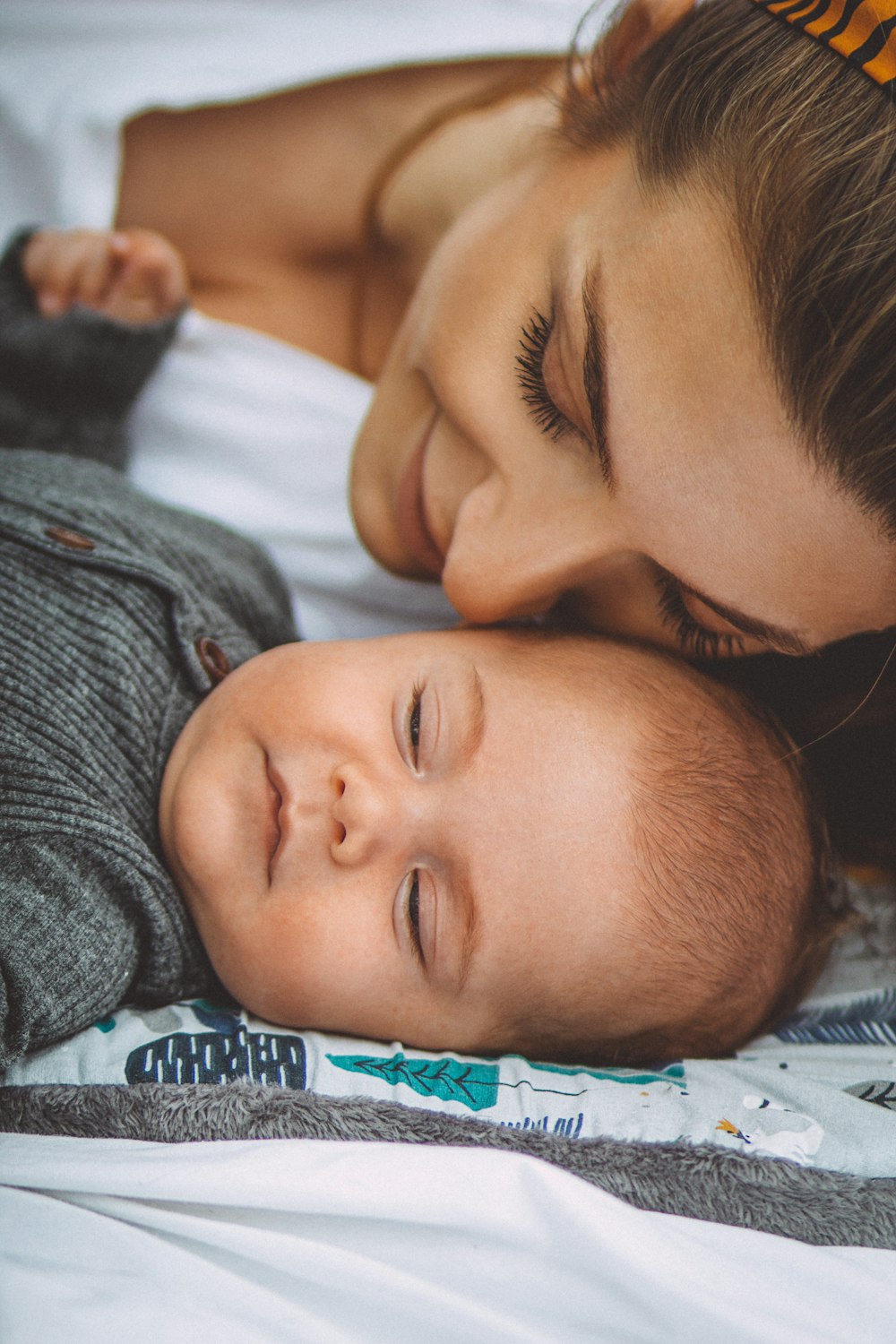 Frau im grauen Hemd liegt neben Baby auf dem Bett