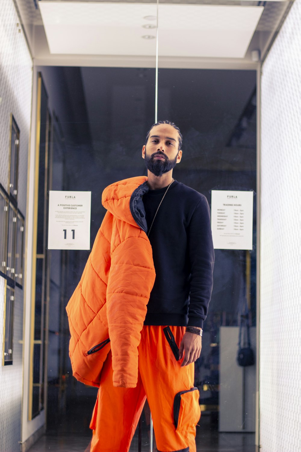 man in black and orange jacket standing near glass window