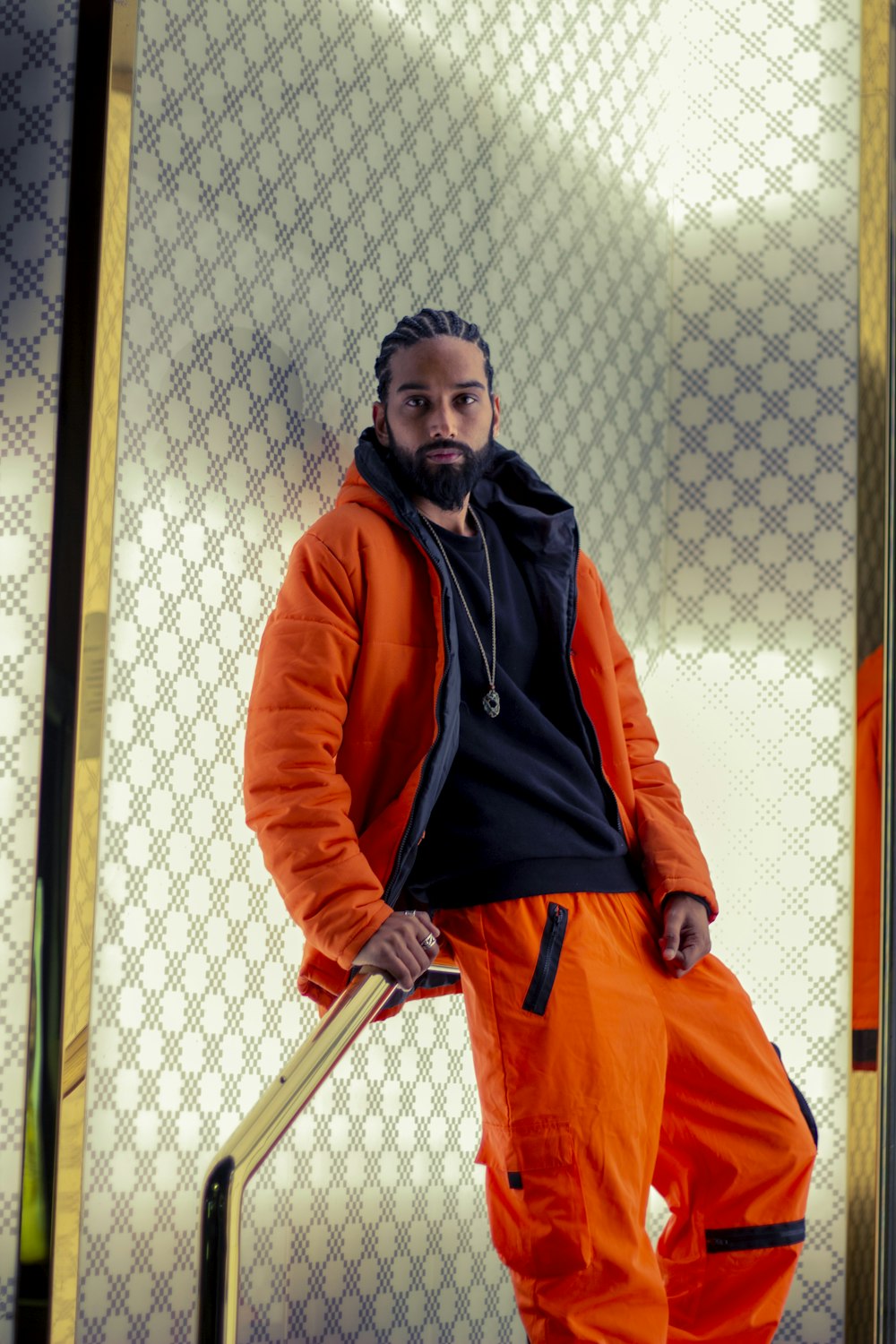 man in orange zip up jacket standing beside white wall