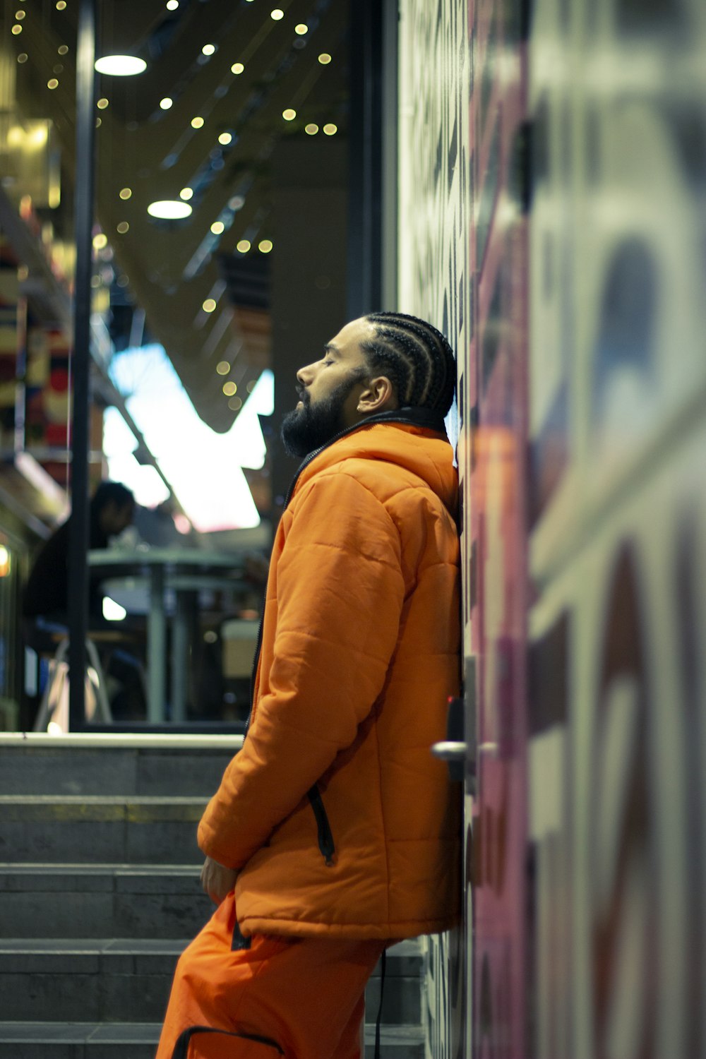 man in orange jacket standing in front of glass window