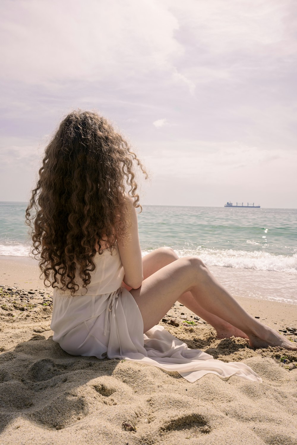 낮 동안 해변에 앉아 하얀 드레스를 입은 여자