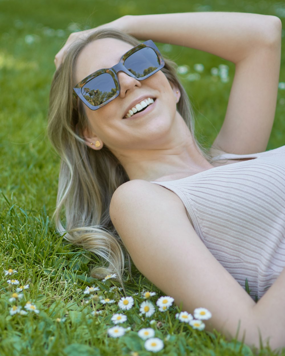 woman in white and black stripe tank top wearing blue sunglasses lying on green grass field