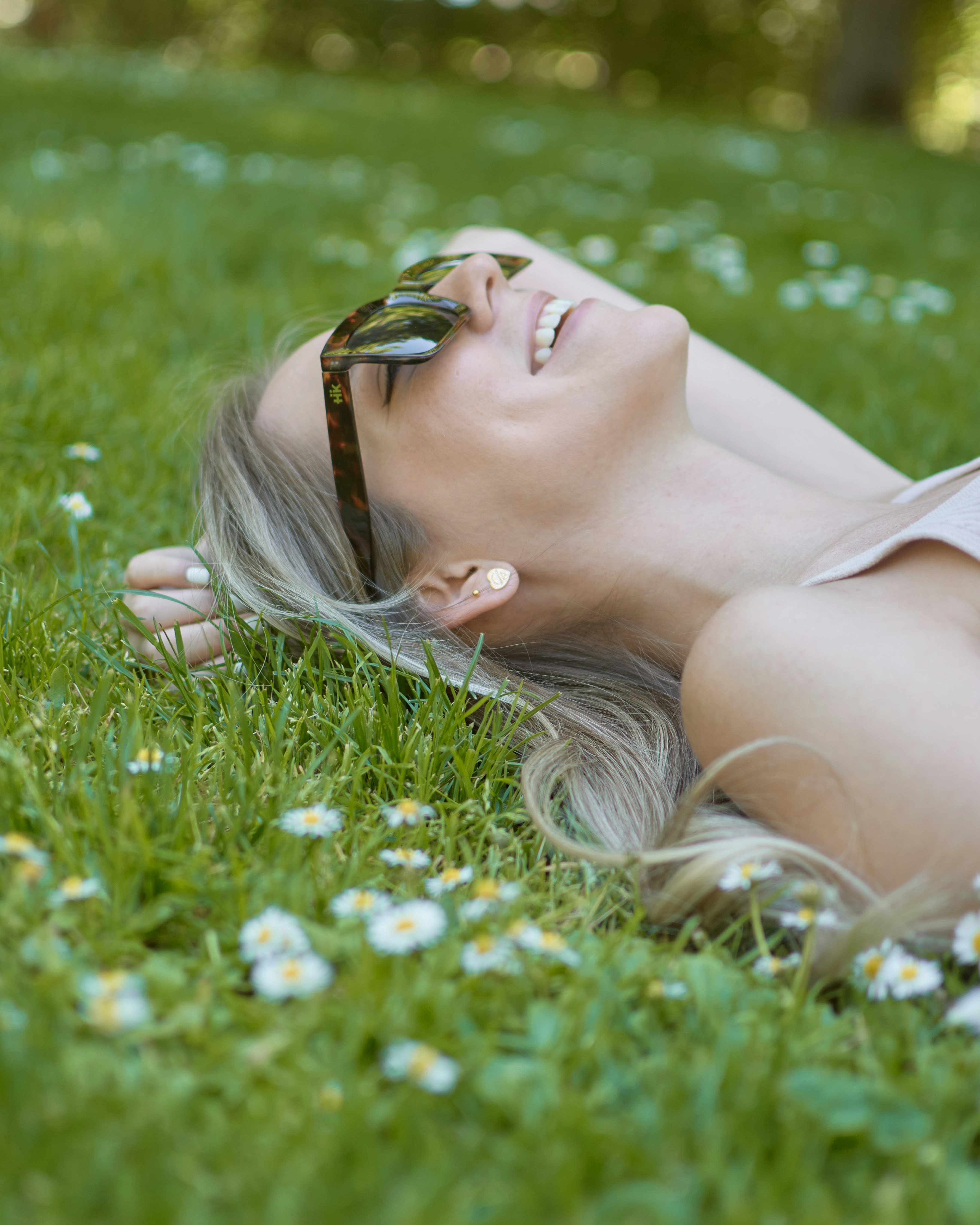woman in white tank top lying on green grass field during daytime