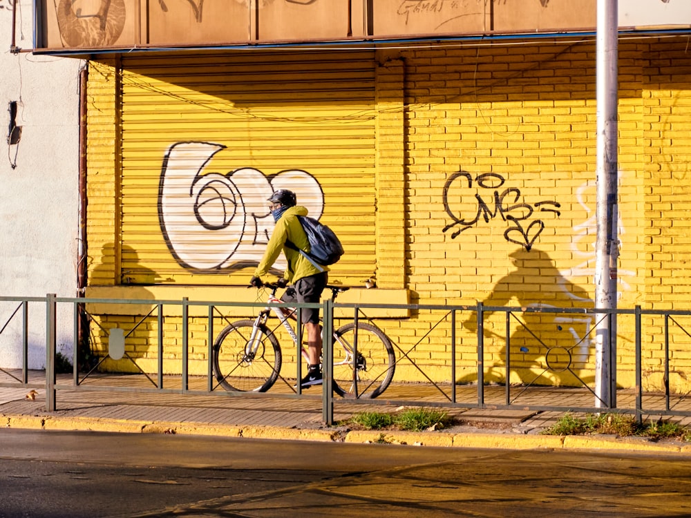 a man riding a bike down a street past a yellow wall