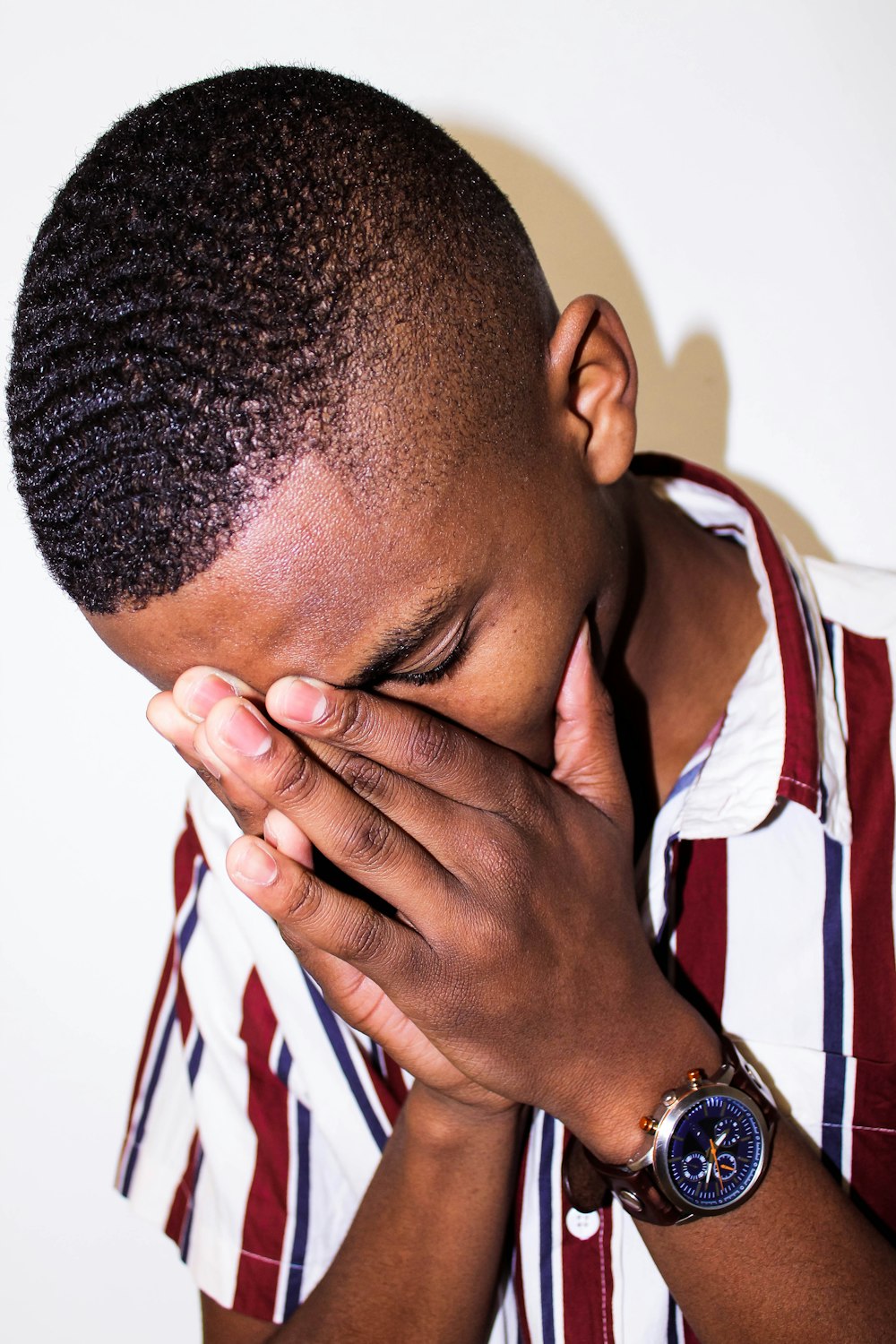 man in white red and black stripe polo shirt covering his face