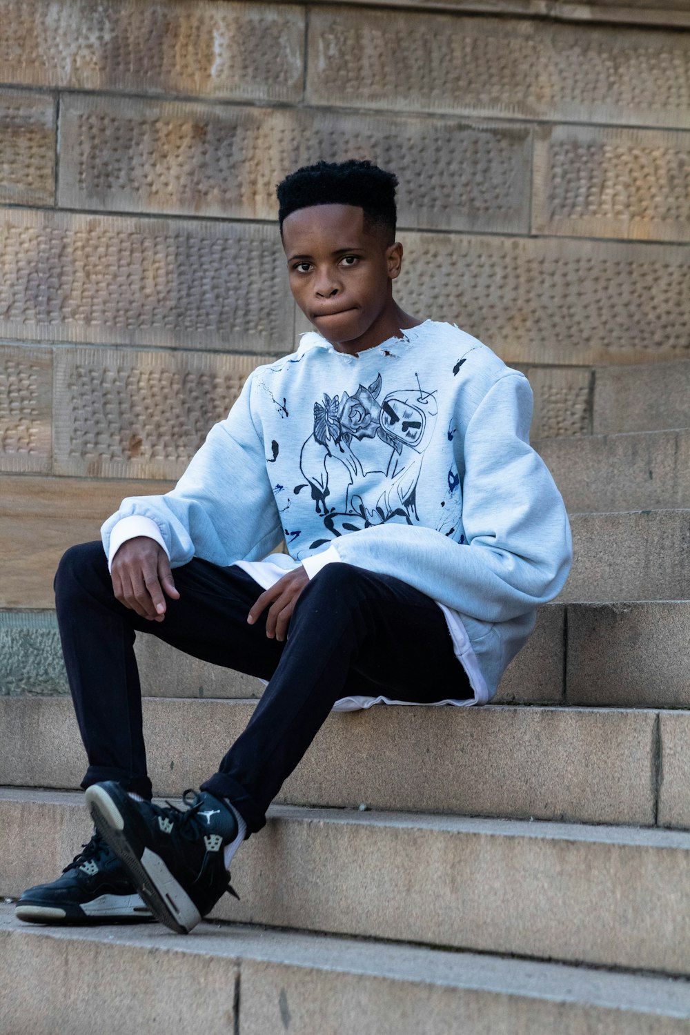 man in white and blue sweater sitting on gray concrete stairs