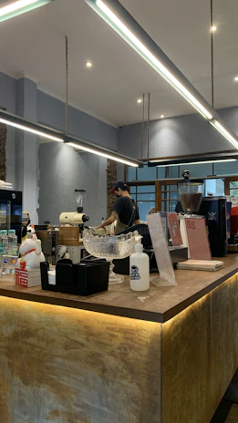A modern cafe owner arranging Airtis water bottles on a sleek counter with soft aqua blue accents.