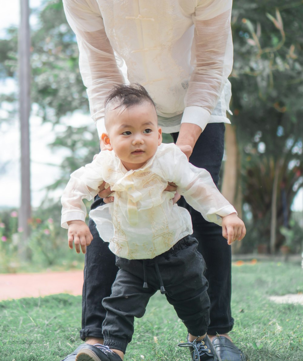baby in white dress shirt and black pants standing on green grass field during daytime