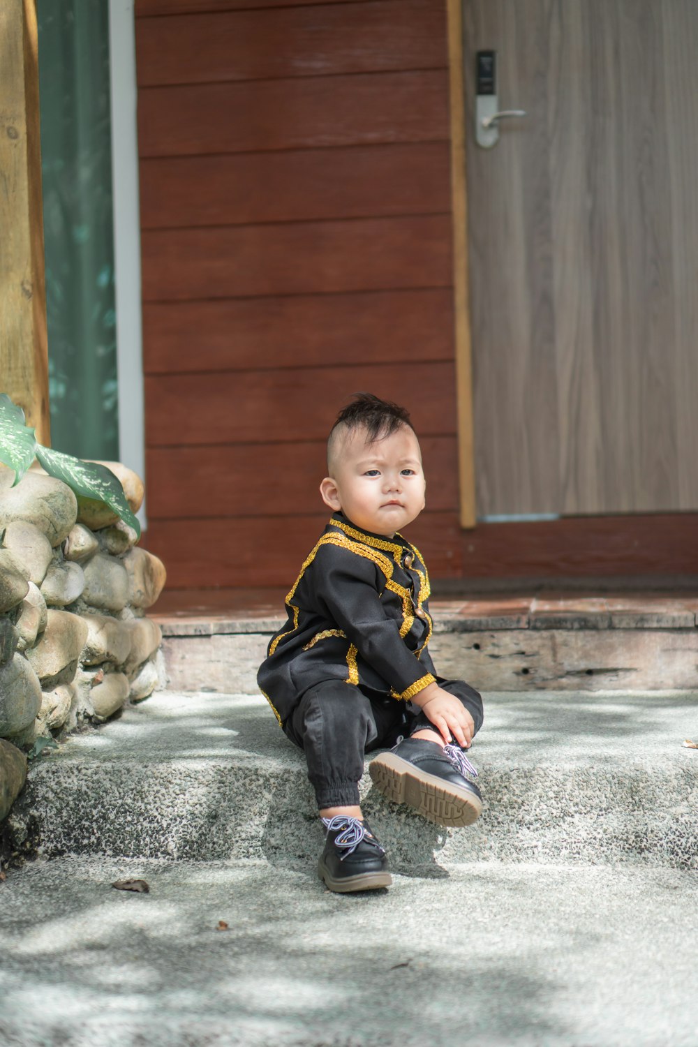 boy in black and yellow jacket sitting on gray concrete floor