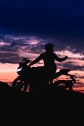 A biker silhouetted against a fiery orange sunset on an open highway.
