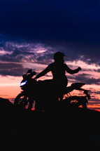 Dark-themed motorcycle rider silhouette against a moody twilight sky.