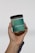 A hand is holding a clear jar with a green label that reads 'GOOD SKIN CLUB BIOME BALANCE 40 BILLION PRE + PROBIOTIC SUPPORT. Supports digestive health and balance. Promotes clear and healthy skin. DIETARY SUPPLEMENT IN CAPSULES.' The jar has a black screw-top lid.