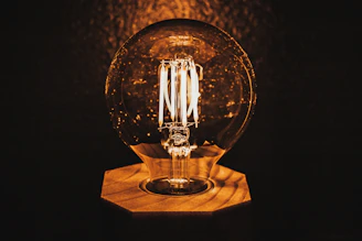 A close-up of a ceramic base desk lamp glowing warmly on a wooden desk.