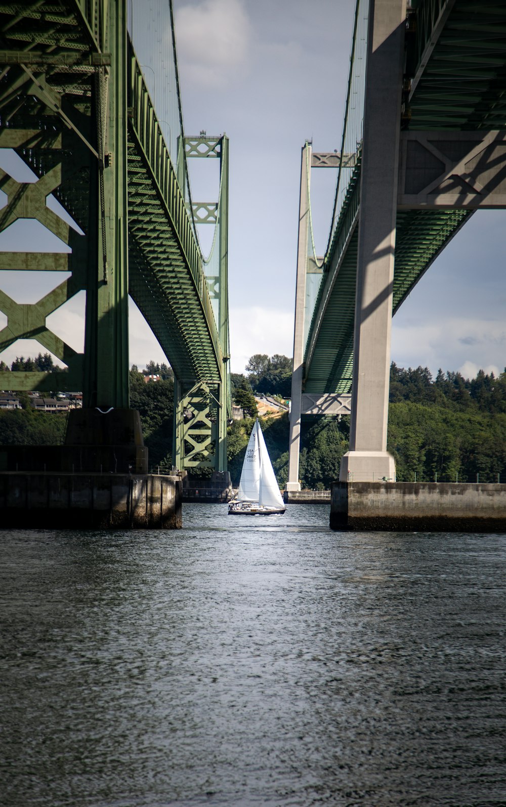 weißes Segelboot tagsüber auf dem Wasser unter der Brücke