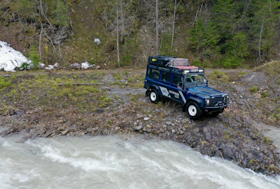 4x4 vehicle parked near a river with mountains in the background.