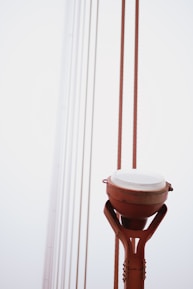 A close-up view of an orange structural element that appears to be part of a large bridge, with thick cables leading upwards into the foggy sky.
