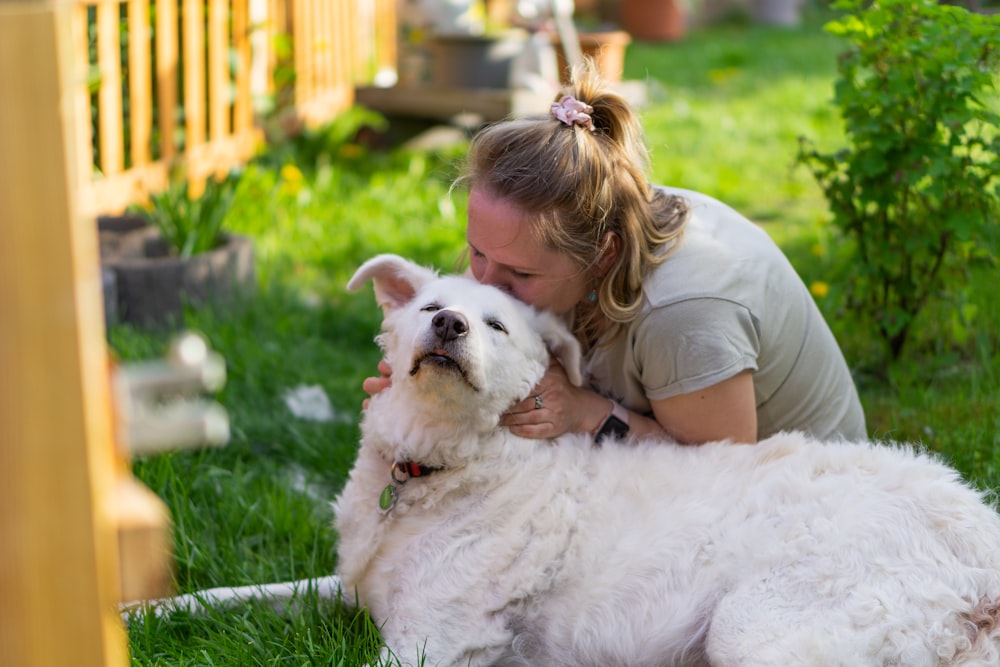 girl in brown shirt lying on white dog on green grass during daytime