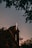 A brick church with a prominent illuminated cross atop its roof, surrounded by silhouetted trees against a dusky sky.