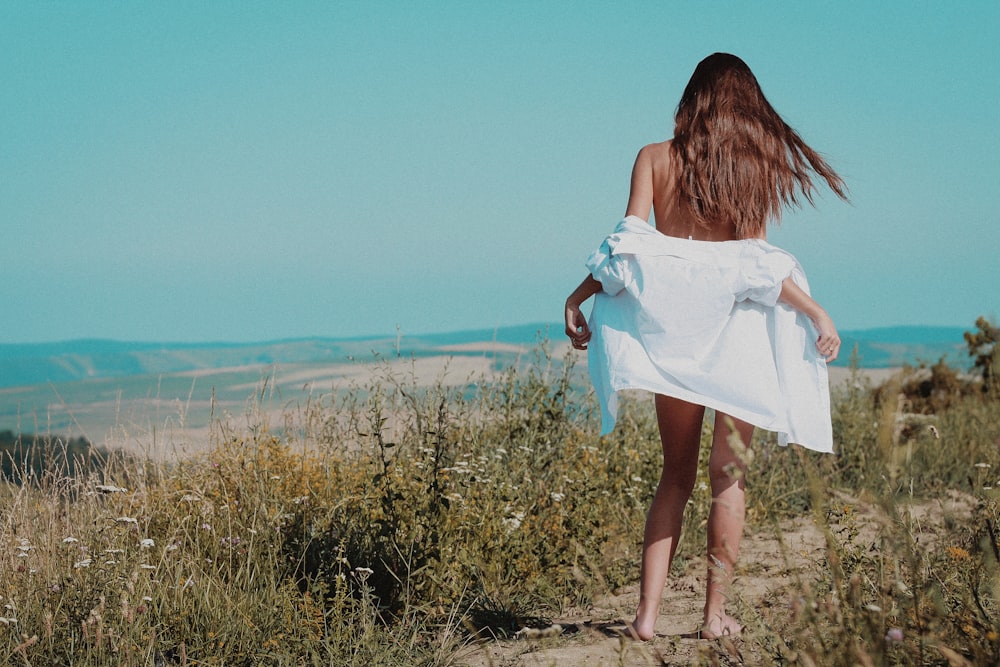 femme en robe blanche marchant sur le champ d’herbe verte pendant la journée