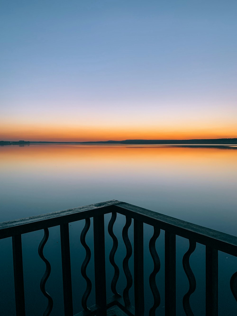 black wooden railings near body of water during sunset