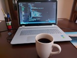 A laptop displaying code with a coffee cup beside it.