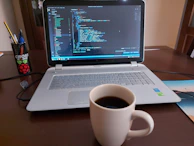 Hands typing code on a laptop with a coffee cup nearby.