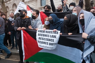 man in black jacket and black cap holding white banner