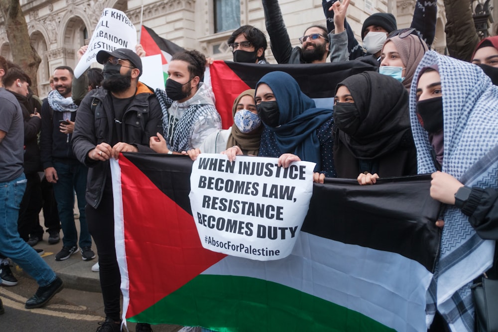 man in black jacket and black cap holding white banner