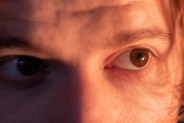 A close-up of a human face focusing on the eyes. The image captures the texture of the skin and the detail of the eyelashes and eyebrows, with a warm lighting that highlights the facial features.