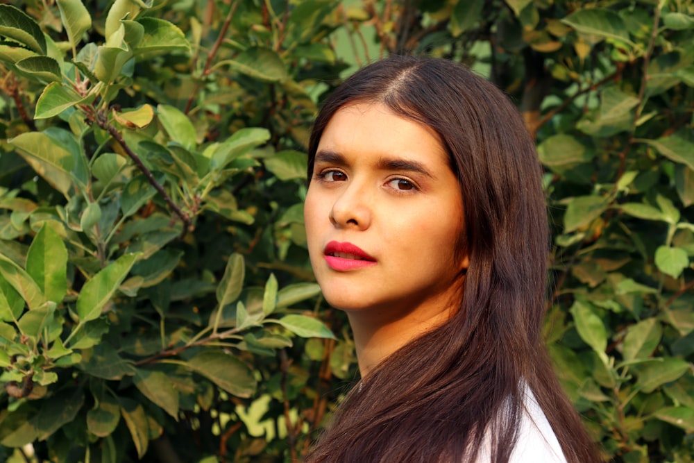 woman in white shirt standing beside green plant