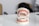 A dental model displaying a set of teeth with orthodontic braces on both the upper and lower jaws. The model is positioned on a glossy white surface with a blurred background. Soft lighting highlights the dental features.