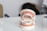 A dental model displaying a set of teeth with orthodontic braces on both the upper and lower jaws. The model is positioned on a glossy white surface with a blurred background. Soft lighting highlights the dental features.