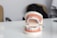 A dental model displaying a set of teeth with orthodontic braces on both the upper and lower jaws. The model is positioned on a glossy white surface with a blurred background. Soft lighting highlights the dental features.