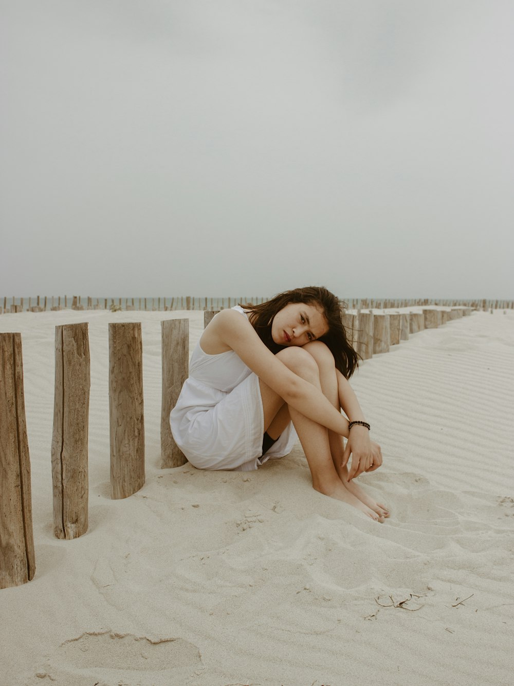 Mujer en vestido blanco sentada en arena blanca durante el día