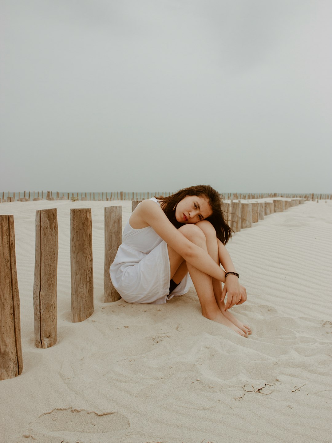 woman in white dress sitting on white sand during daytime