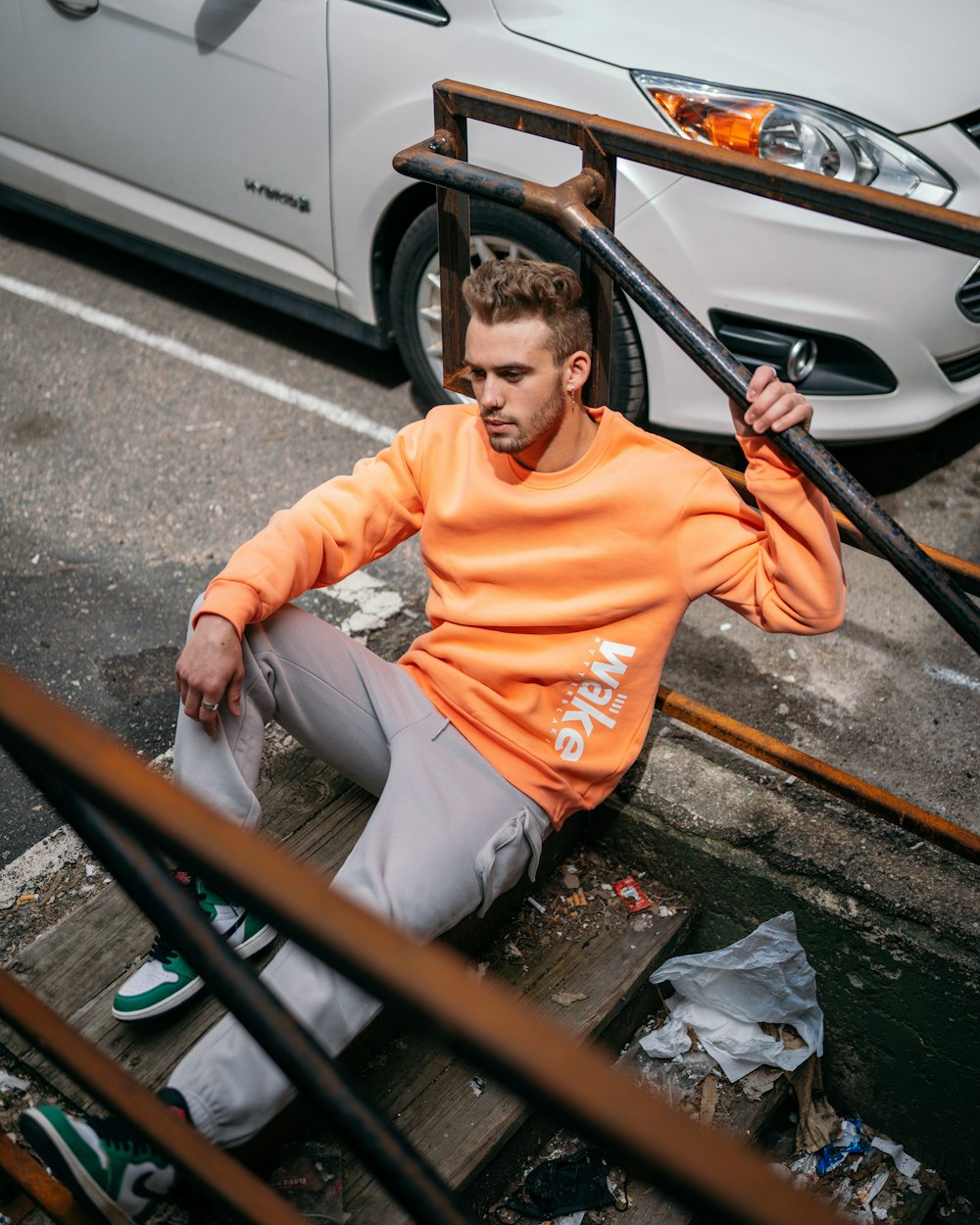 man in orange crew neck t-shirt and gray pants sitting on black steel railings