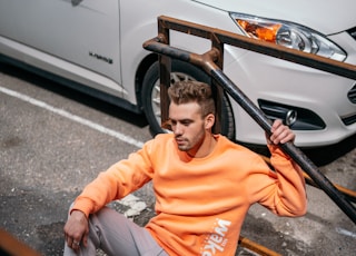 man in orange crew neck t-shirt and gray pants sitting on black steel railings