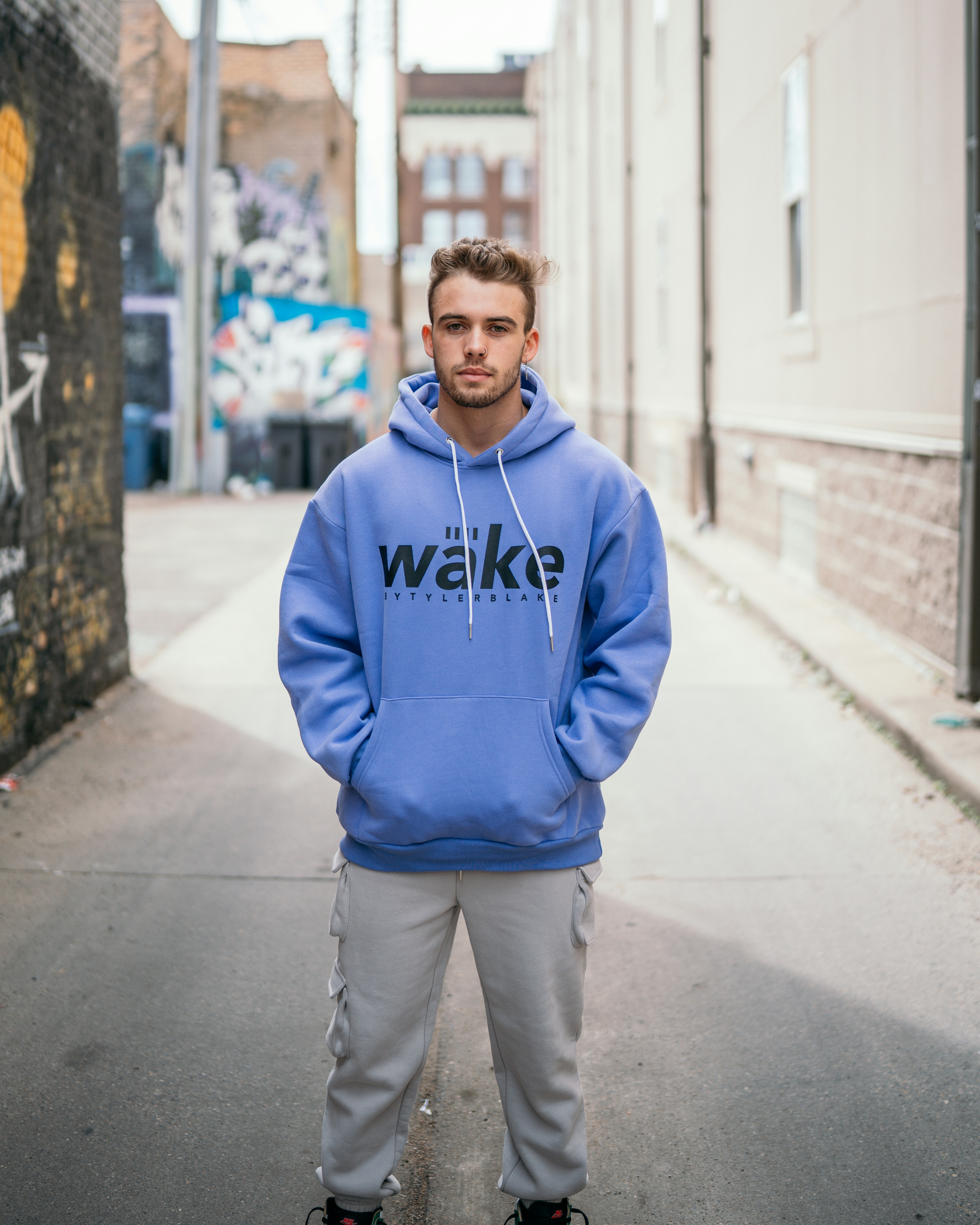 man in blue and white pullover hoodie standing on sidewalk during daytime