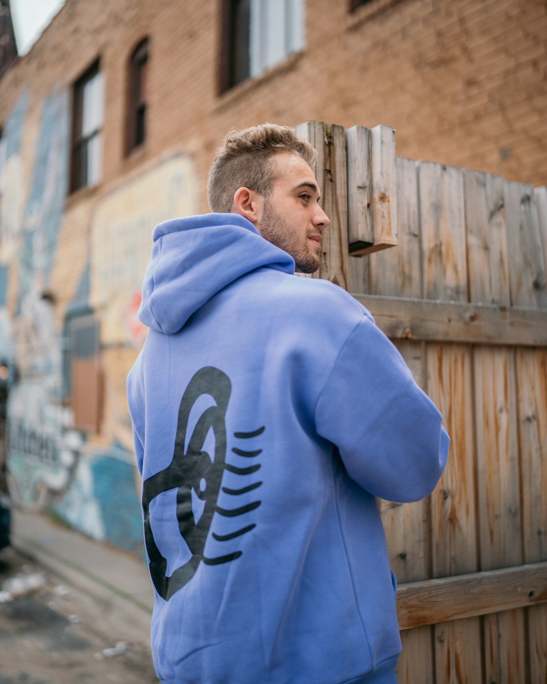 man in blue and white hoodie standing near brown wooden fence during daytime