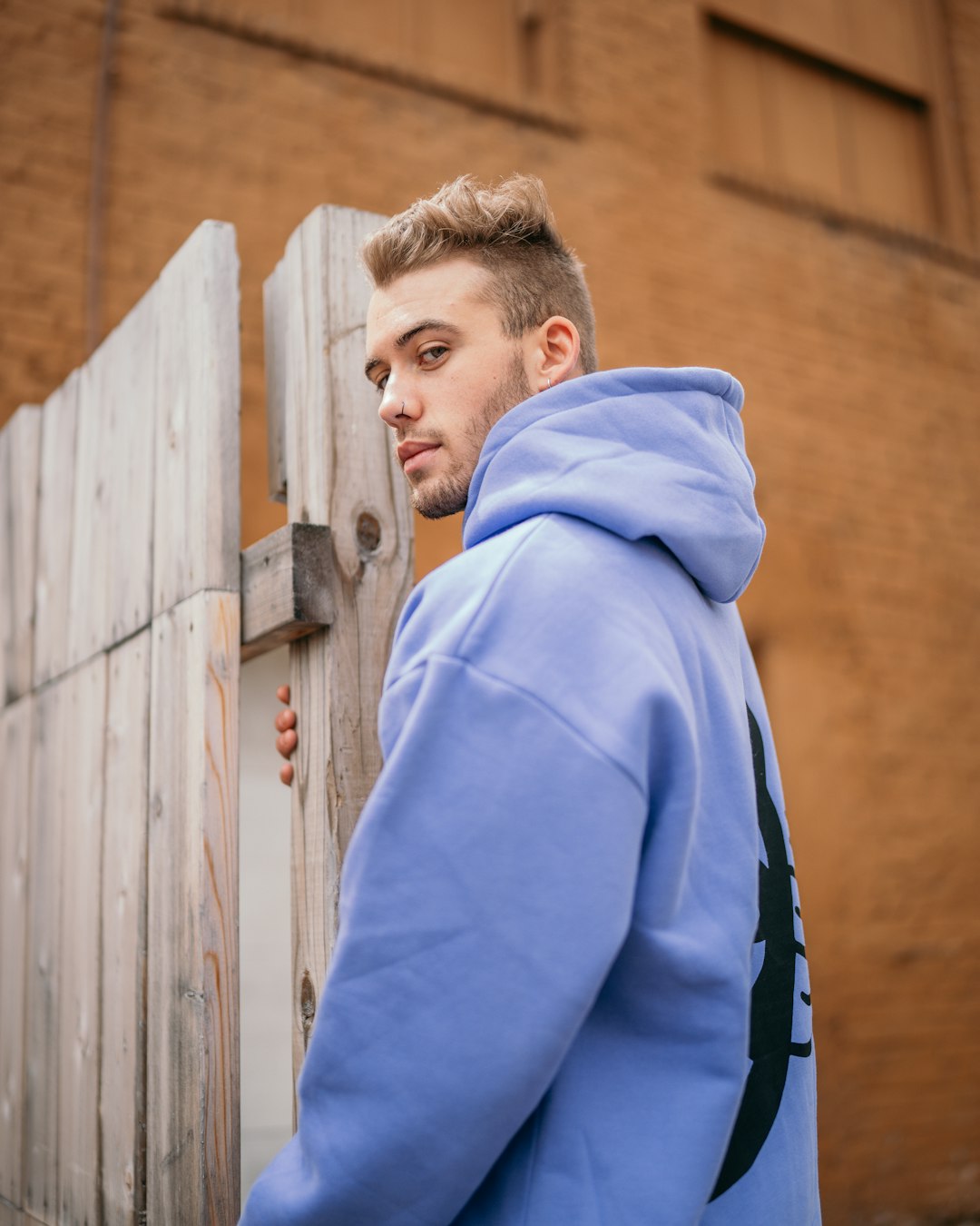 man in blue hoodie standing beside brown wooden fence