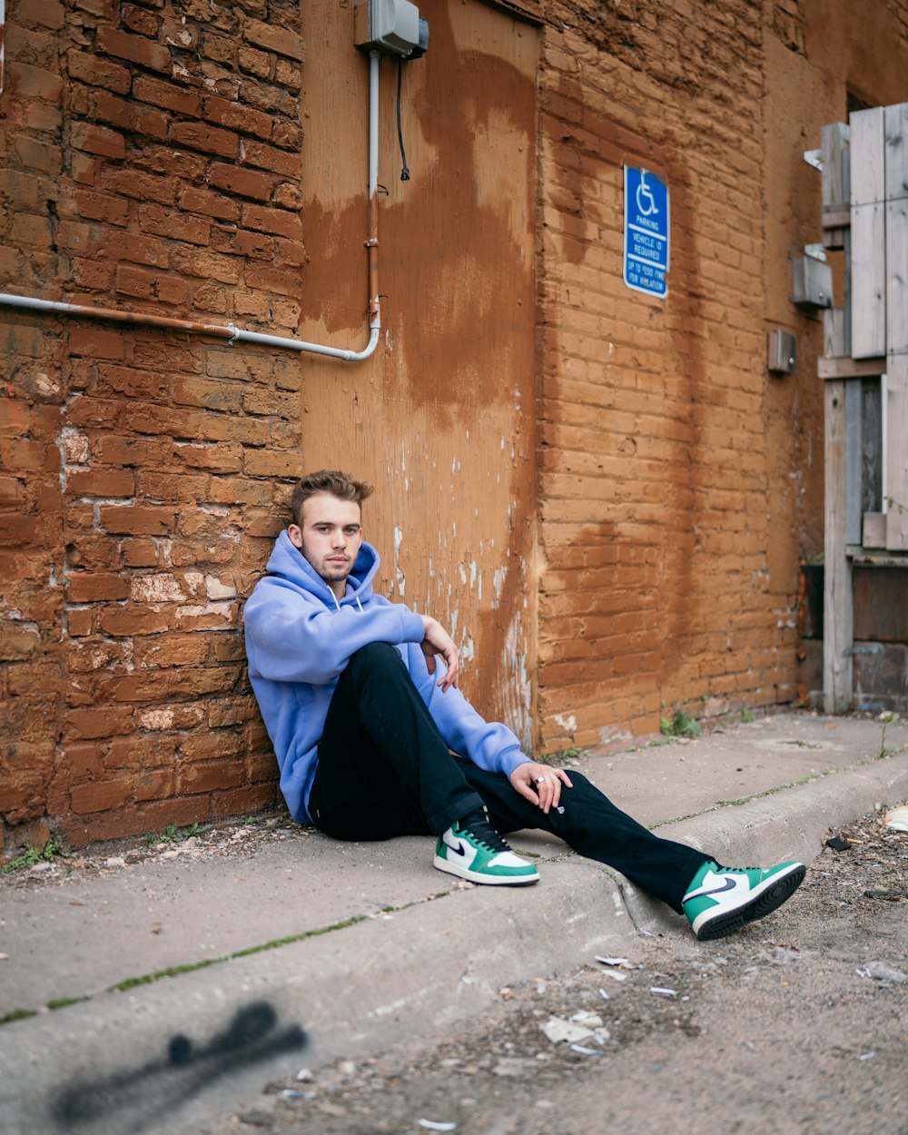 woman in blue jacket and blue pants sitting on sidewalk during daytime