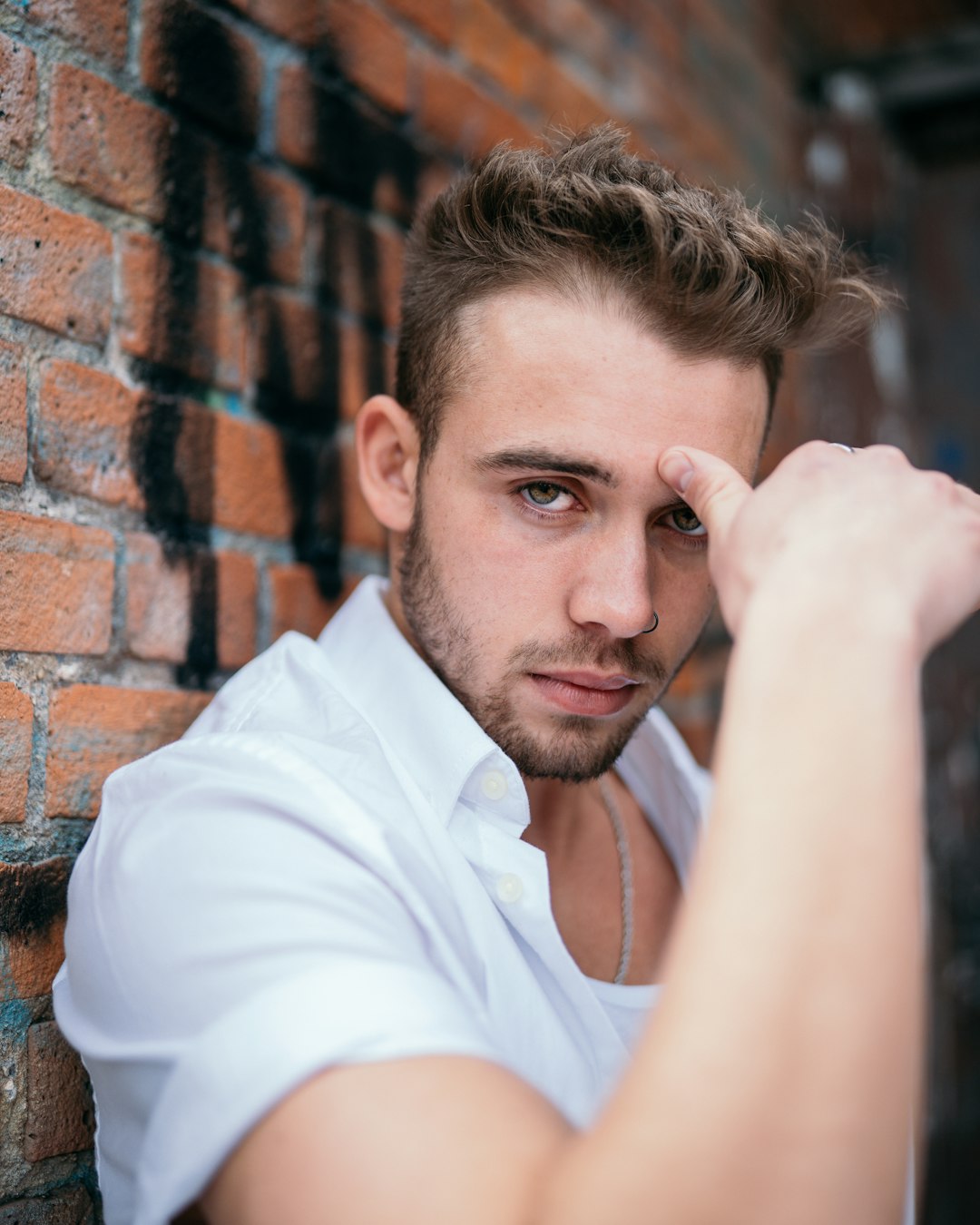 man in white button up shirt leaning on brown brick wall